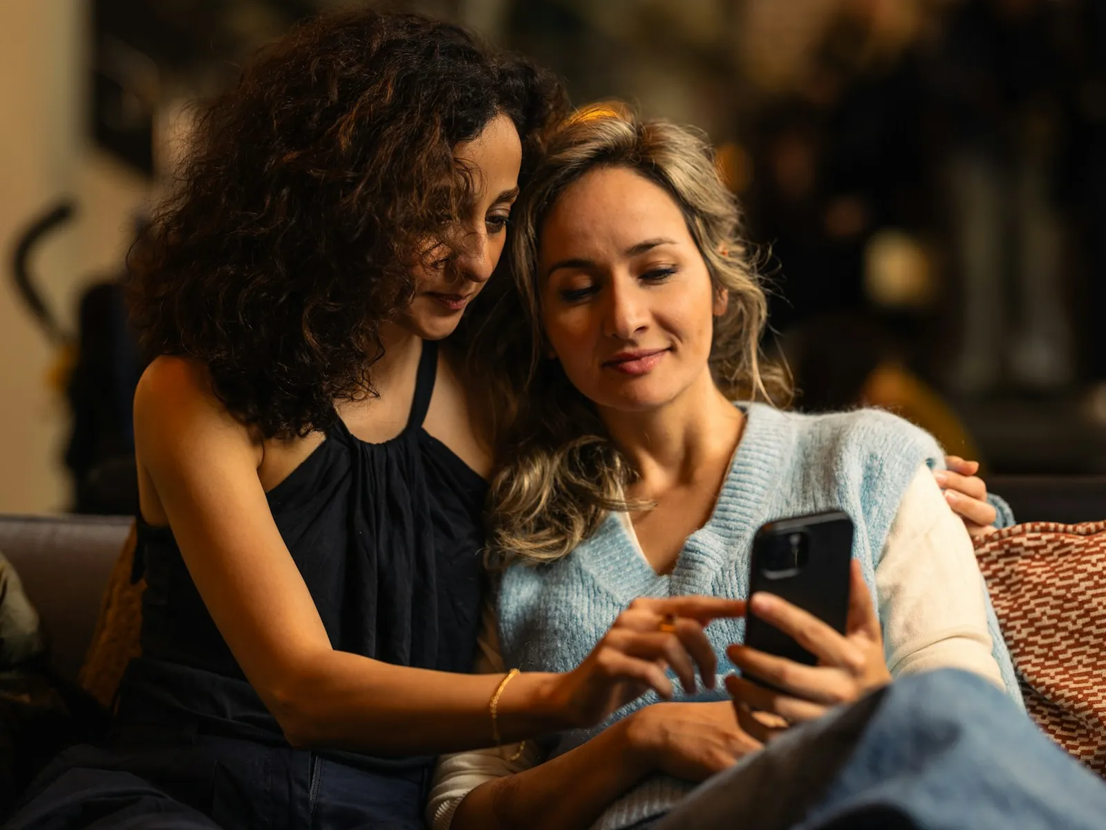Une femme montre son téléphone à une amie, sur un canapé