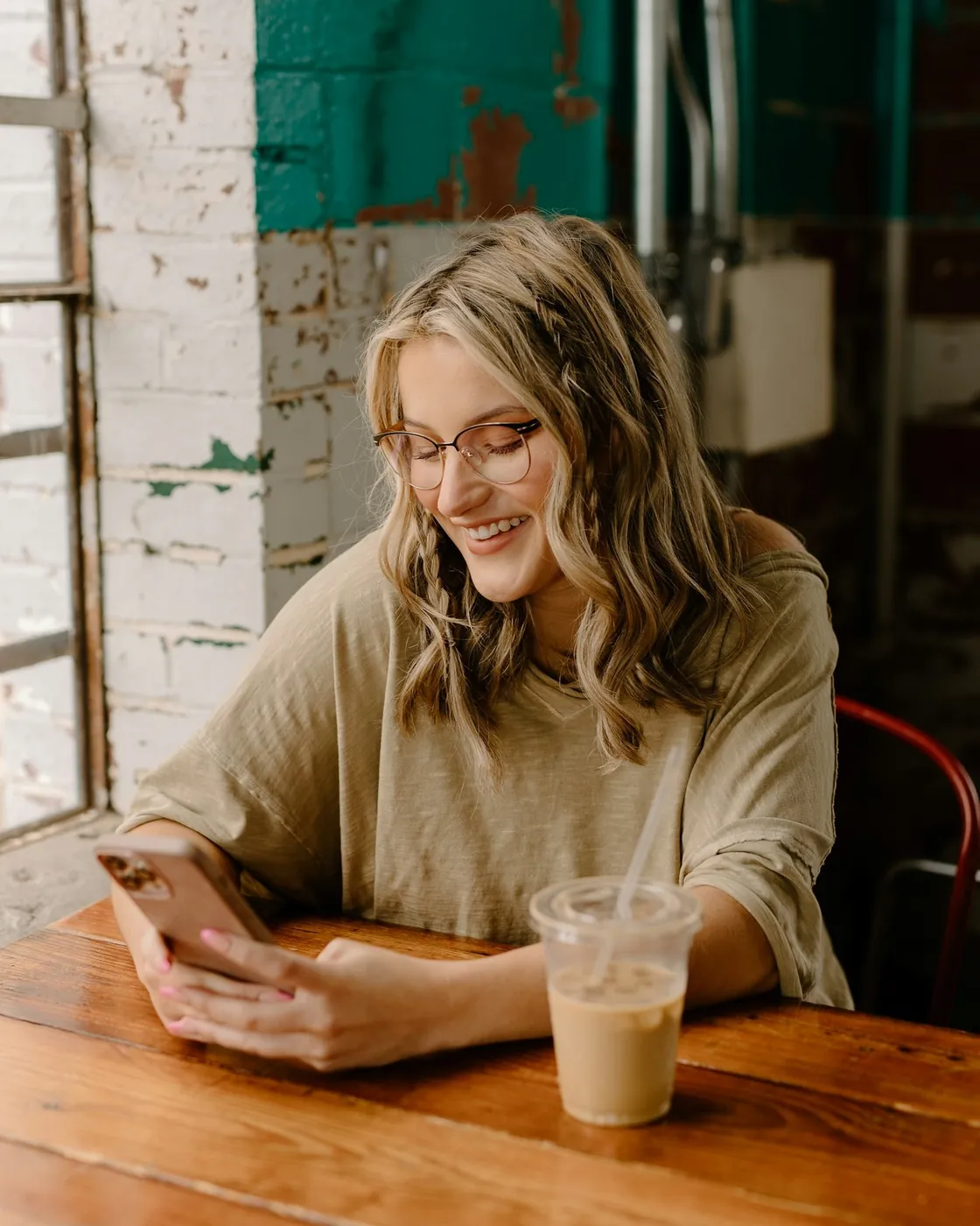 Une femme sourit en regardant son téléphone, à la table d'un café